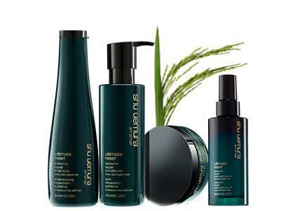 A group of Shu Uemura Ultimate Reset hair care products, including shampoo, conditioner, mask, serum, and spray, with green packaging and a plant in the background.