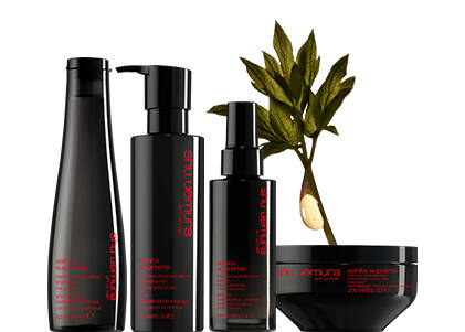 Shu Uemura products in black packaging, including bottles and a jar, displayed alongside a plant with a droplet of oil.