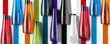 Colorful bottles of Shu Uemura shampoos arranged against vertical stripes of red, blue, green, and orange.