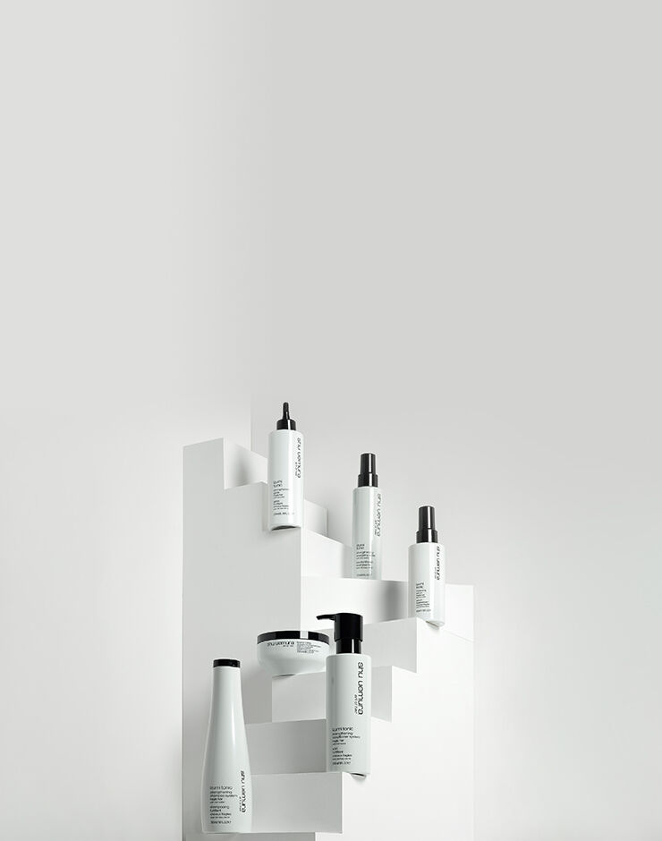 Four black bottles of Shu Uemura Ashita Supreme intense revitalization haircare products, including shampoo, conditioner, mask, and spray, displayed on a black and red gradient background.
