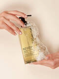 Hands holding a bottle of Shu Uemura Gentle Radiance Deep Cleanser weightless shampoo with foam and bubbles surrounding the bottle.
