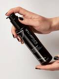 Hands holding a bottle of Shu Uemura Gentle Radiance Deep Cleanser weightless shampoo with foam and bubbles surrounding the bottle.