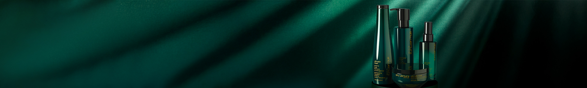 Three green bottles of Shu Uemura Ultimate Reset hair care products on a dark green background with light streaks.