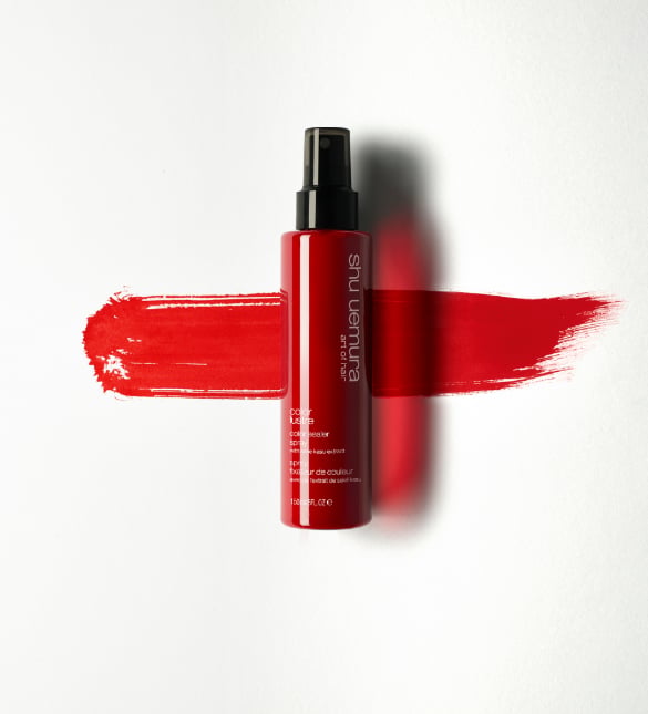 A person holds a red bottle of Shu Uemura Blow Dry Oil Spray, showcasing a tattooed arm.