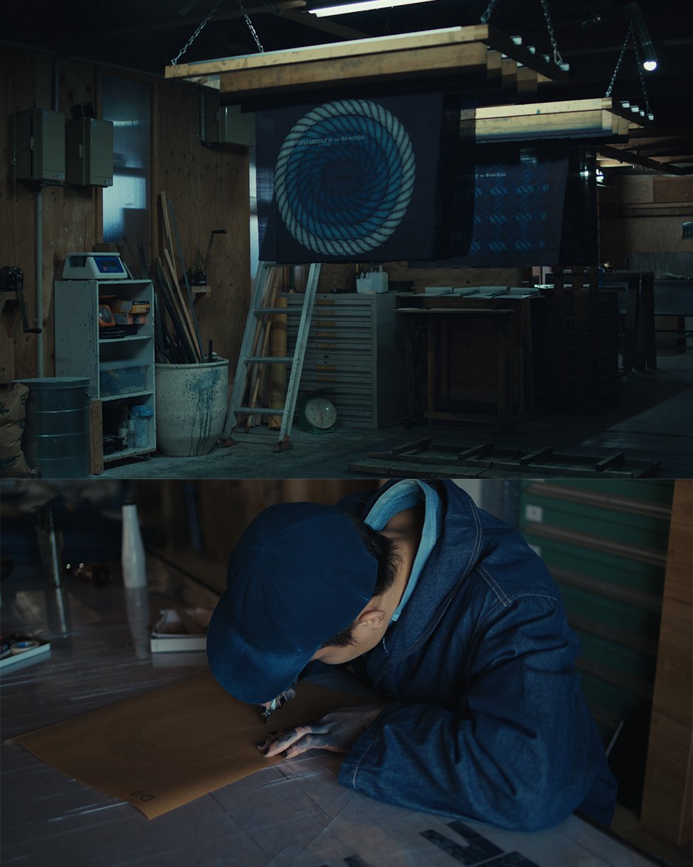 shu uemura art of hair limited-edition holiday gift sets A workshop with hanging indigo-dyed fabrics featuring rope and geometric designs, tools, and equipment in the background. Below, a person in a blue cap and denim jacket works on a design at a table.