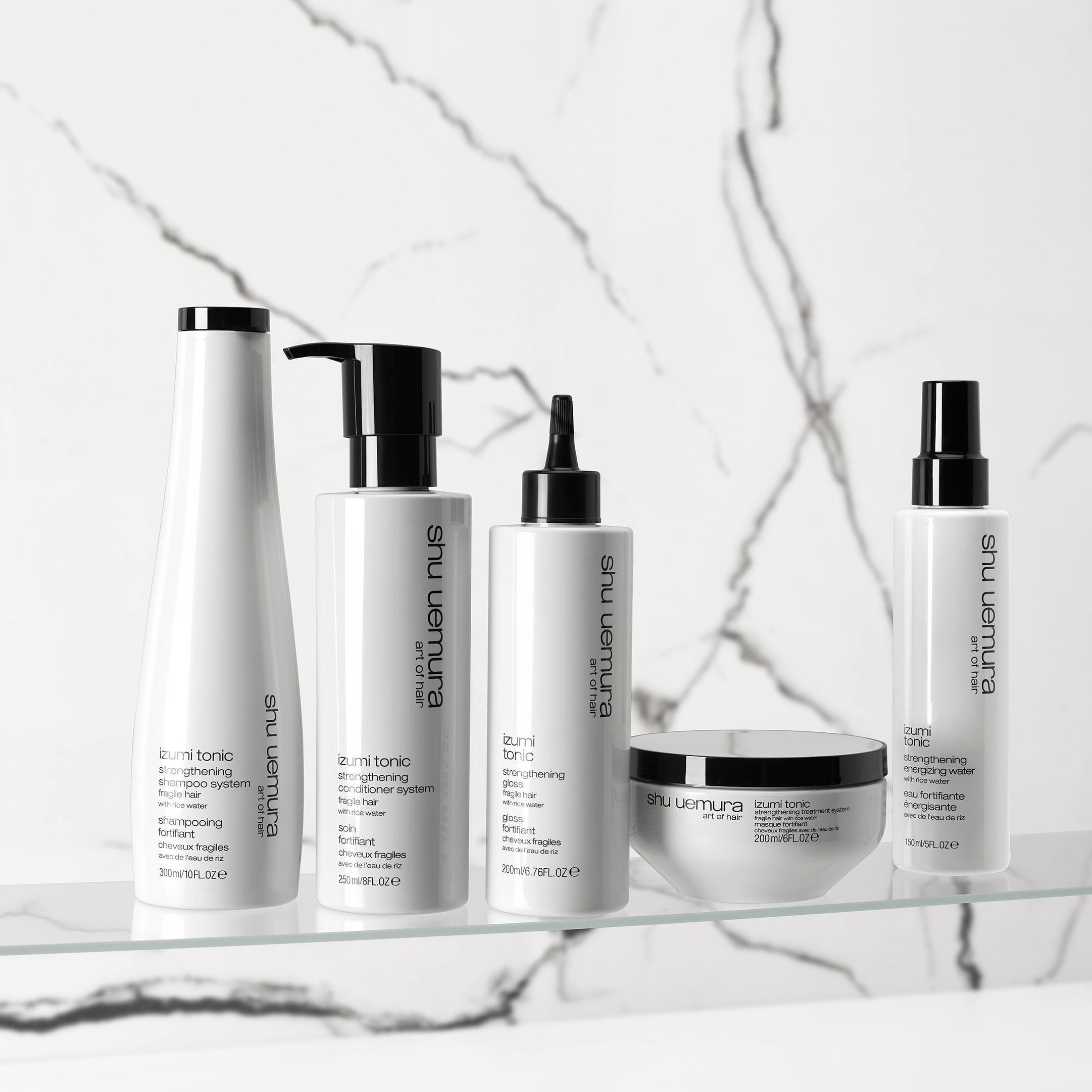 Shu Uemura Izumi Tonic hair care products displayed on a white platform, including bottles, a jar, and a spoon with rice grains.